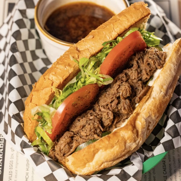 A Cavalier pub sandwich with shredded meat, lettuce, and tomato, served with a side of au jus.