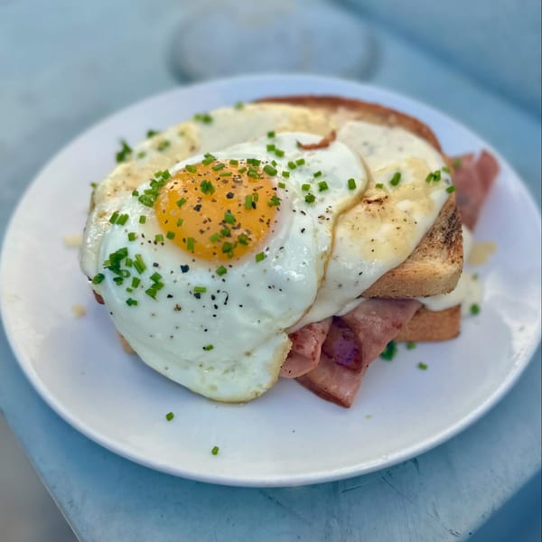 A Cavalier Croque Madame with fried eggs, ham, and chives on a white plate.