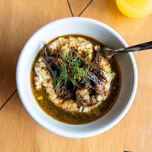 A bowl of shrimp and grits with a rich sauce, garnished with fresh dill, on a wooden table.