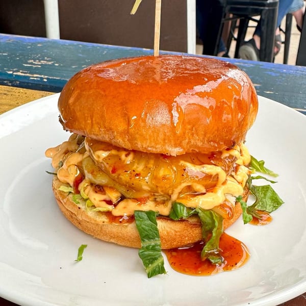 A Cavalier pub burger with a shiny bun, sauce, lettuce, and a wooden skewer.