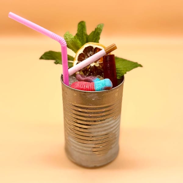 A cocktail in a tin can, garnished with mint, dried orange, candy, and a pink straw.
