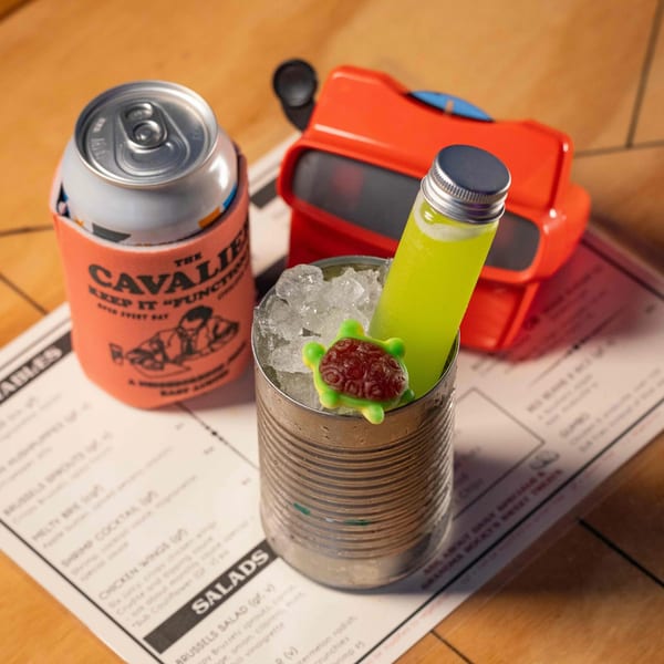 A Cavalier koozie with a can, a green cocktail in a tin can, and a red View-Master.