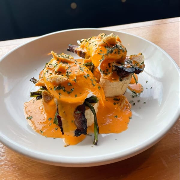 Eggs Benedict with bright orange hollandaise sauce and green herbs on a white plate.