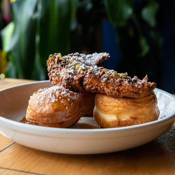 Fried chicken and two beignets drizzled with syrup and powdered sugar on a white plate.