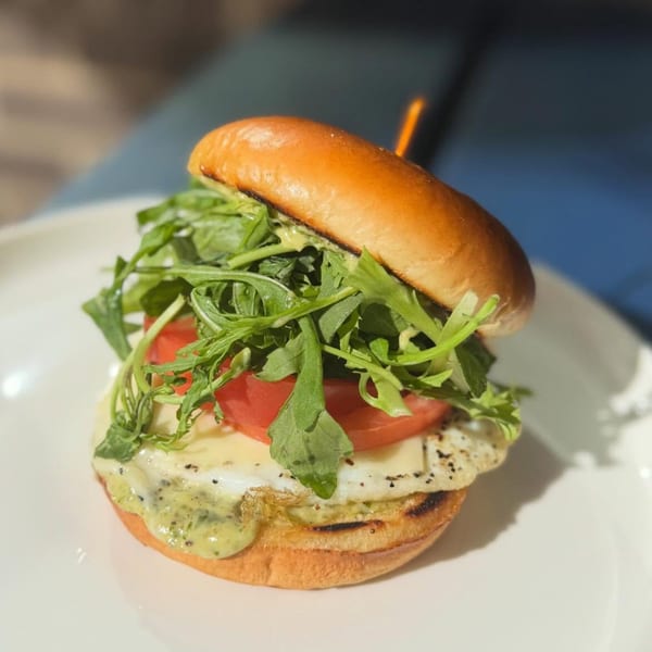 A burger with arugula, tomato, melted cheese, and green sauce on a toasted bun.