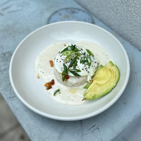 A white bowl of biscuits and gravy topped with a poached egg, avocado, and green onions.